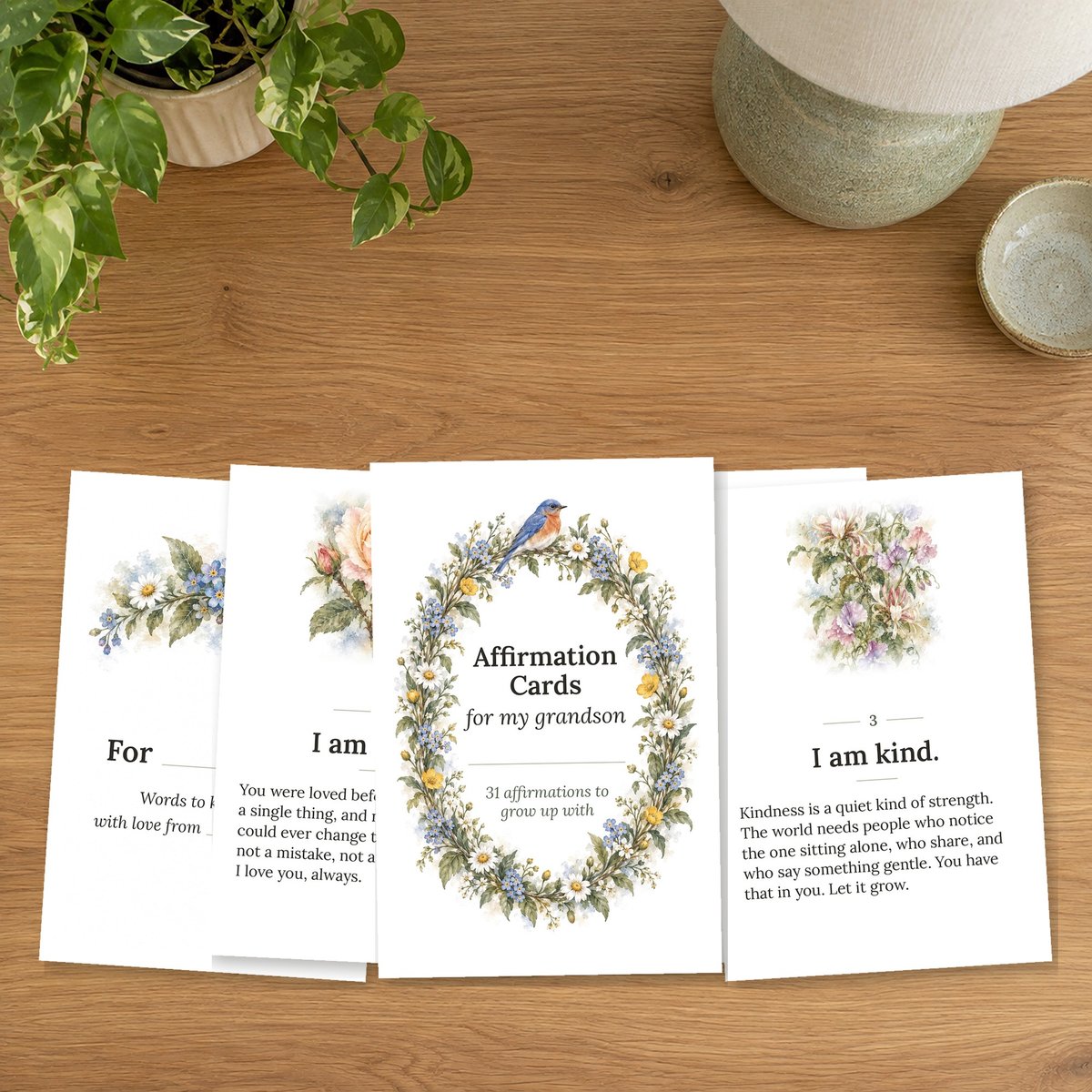 A fan of printable affirmation cards on a bedside table with a lamp and a plant